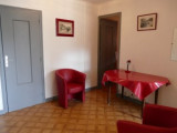 Un hall d’entrée avec un parquet en bois, meublé d'une table recouverte d'une nappe rouge et de deux fauteuils assortis.