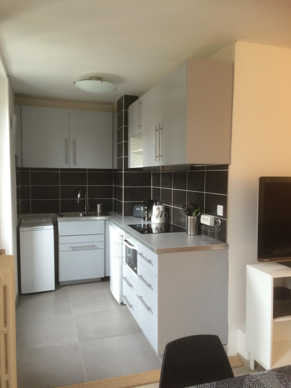 Cuisine équipée en L avec lave-linge, frigo, bouilloire et grille-pain.